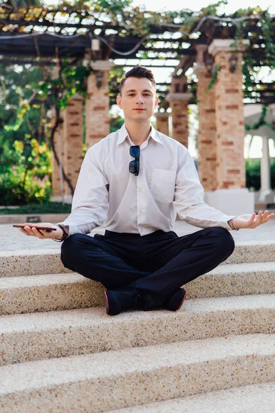 Onun telefon tutarak ve lotus açık havada merdivenlerde oturan genç işadamı poz