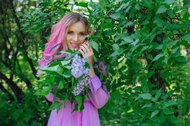 Güzel moda model kızla renkli boyalı saç ve Lila bush ve holding eflatun çiçekler yanında mükemmel makyaj ve saç standig