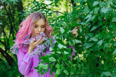 Güzel moda model kızla renkli boyalı saç ve Lila bush ve holding eflatun çiçekler yanında mükemmel makyaj ve saç standig