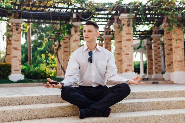 Onun telefon tutarak ve lotus açık havada merdivenlerde oturan genç işadamı poz