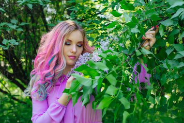 Güzel moda model kızla renkli boyalı saç ve Lila bush ve holding eflatun çiçekler yanında mükemmel makyaj ve saç standig