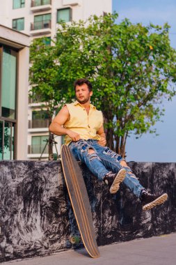 Sakallı, genç ve yakışıklı bir adam sokakta uzun tahtayla oturuyor..