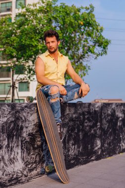 Sakallı, genç ve yakışıklı bir adam sokakta uzun tahtayla oturuyor..