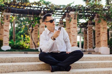 Onun telefon tutarak ve tropikal bir ülkede açık havada merdivenlerde oturan genç işadamı