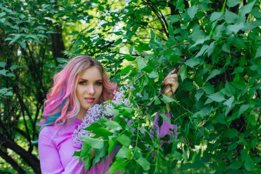 Güzel moda model kızla renkli boyalı saç ve Lila bush ve holding eflatun çiçekler yanında mükemmel makyaj ve saç standig