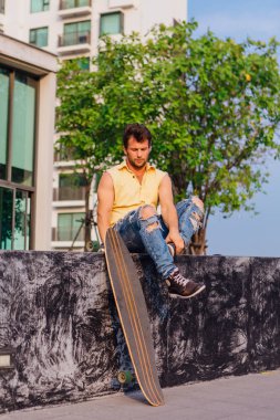 Sakallı, genç ve yakışıklı bir adam sokakta uzun tahtayla oturuyor..