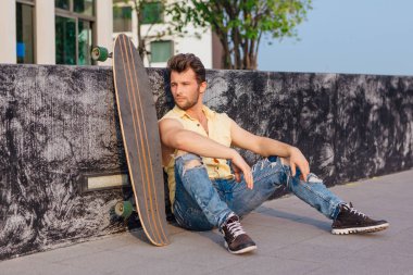 Sakallı, genç ve yakışıklı bir adam sokakta uzun tahtayla oturuyor..