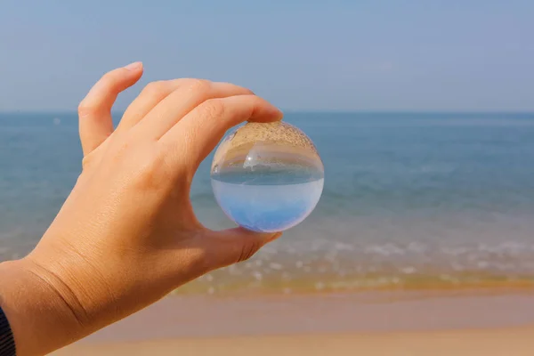 Lens van de bal in de hand met de weerspiegeling van de zee en de zonsondergang op het strand — Stockfoto