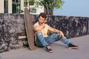 İle longboard sokakta oturan genç adam.