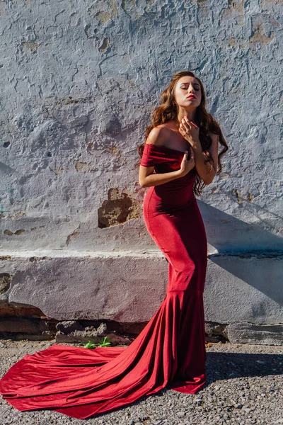 Güzel genç kadın yanındaki duvar eski bir tren konumu olan bir uzun kırmızı gece elbisesi içinde. Kopya alanı