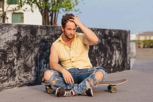 Sakallı longboard sokakta oturan genç yakışıklı adam.