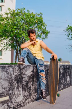 Sakallı, genç ve yakışıklı bir adam sokakta uzun tahtayla oturuyor..