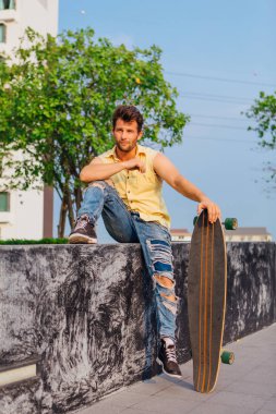 Sakallı, genç ve yakışıklı bir adam sokakta uzun tahtayla oturuyor..