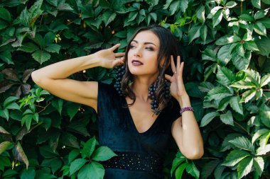 Siyah üzüm bir küpe gibi tutarak siyah elbiseli Genç Seksi esmer portresi.