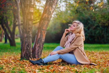 Düşen sarı sonbahar ile zemin örtmek ağacın altında oturan genç güzel kadın bırakır