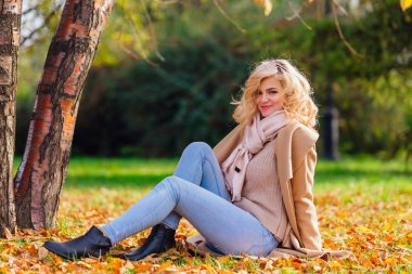 Düşen sarı sonbahar ile zemin örtmek ağacın altında oturan genç güzel kadın bırakır