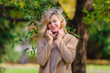 Güzel zarif sarışın kadın ceket ayakta sonbahar park ağaç altında giyinmiş. Güneşli Ekim gün.