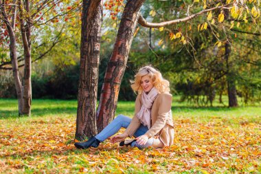 Zemin örtmek ile düşmüş sonbahar üzerinde oturan genç güzel kadın bırakır