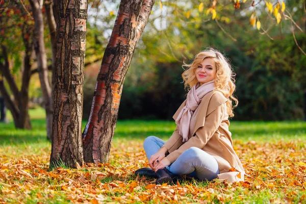 Молода красива жінка сидить на землі таємно з осіннім листям — стокове фото