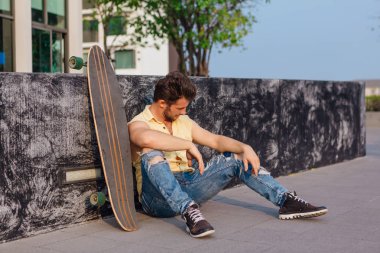 Sakallı, genç ve yakışıklı bir adam sokakta uzun tahtayla oturuyor..