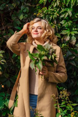 Parkta vahşi üzüm sonbahar buket holding arka plan yanındaki güzel kadın kazak ve ceket durumda Yuong bırakır