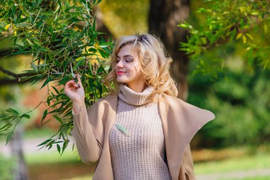 Güzel zarif sarışın kadın ceket ayakta sonbahar park ağaç altında giyinmiş. Güneşli Ekim gün.