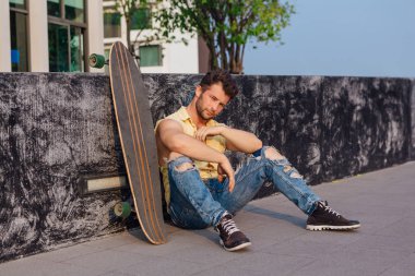Sakallı, genç ve yakışıklı bir adam sokakta uzun tahtayla oturuyor..