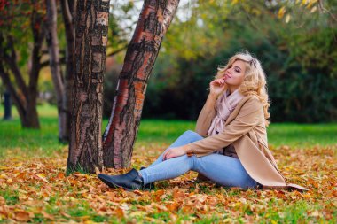 Düşen sarı sonbahar ile zemin örtmek ağacın altında oturan genç güzel kadın bırakır