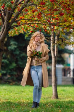 Güzel zarif sarışın kadın ceket ayakta rowanberries ve yaprakları oluşan sonbahar park holding üvez ağacının altında giyinmiş. Güneşli Ekim gün.