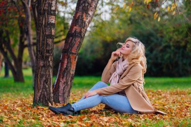 Düşen sarı sonbahar ile zemin örtmek ağacın altında oturan genç güzel kadın bırakır