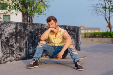 Sakallı longboard sokakta oturan genç yakışıklı adam.