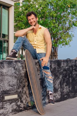 Sakallı, genç ve yakışıklı bir adam sokakta uzun tahtayla oturuyor..