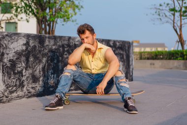 Sakallı longboard sokakta oturan genç yakışıklı adam.