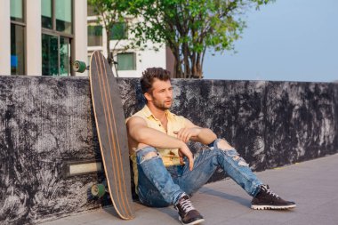 Sakallı, genç ve yakışıklı bir adam sokakta uzun tahtayla oturuyor..