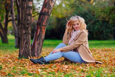 Düşen sarı sonbahar ile zemin örtmek ağacın altında oturan genç güzel kadın bırakır