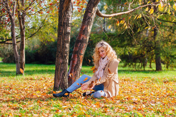 Young beautiful woman sitting under the tree on the ground coverd with fallen yellow autumn leaves