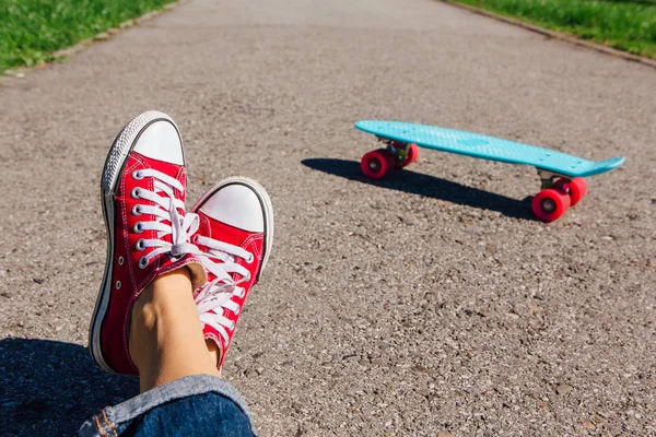 Close up of feet of a girl in red sneakers and blue plastic penny skate board with pink wheels on the background. Urban scene, city life. Sport, fitness lifestyle.