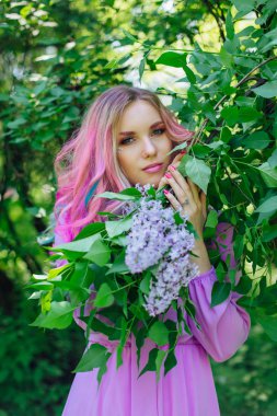 Güzel moda model kızla renkli boyalı saç ve mükemmel makyaj standig leylak bush ve holding eflatun çiçekler yanındaki