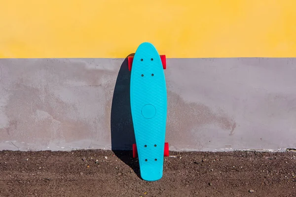 Mavi plastik kaykay kuruş pano pembe tekerlekli duvarın yanında duruyor.