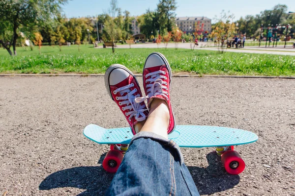 Close up of feet of a girl in red sneakers rides on blue plastic penny skate board with pink wheels. Urban scene, city life. Sport, fitness lifestyle.