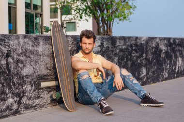 Sakallı, genç ve yakışıklı bir adam sokakta uzun tahtayla oturuyor..