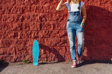 Bir kız kırmızı spor ayakkabılar ve mavi kuruş kaymak kurulu metrelik kadar pembe tekerlekli duvarın yanında ayakta kapatın. Kentsel sahne, şehir hayatı. Spor, fitness yaşam.