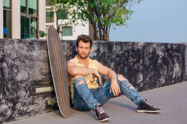 Sakallı, genç ve yakışıklı bir adam sokakta uzun tahtayla oturuyor..