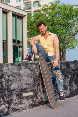 Sakallı, genç ve yakışıklı bir adam sokakta uzun tahtayla oturuyor..