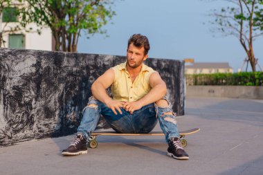 Sakallı longboard sokakta oturan genç yakışıklı adam.