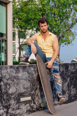 Sakallı, genç ve yakışıklı bir adam sokakta uzun tahtayla oturuyor..