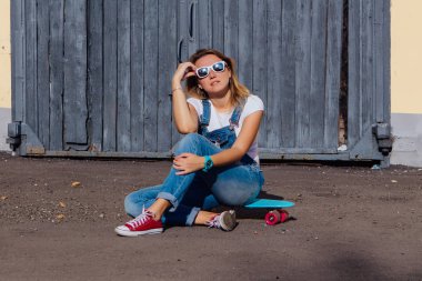 Tulum ve güneş gözlüğü eski ahşap duvar yanında onun kaykay üzerinde oturan giymiş bir gülümseyen kadın portresi.