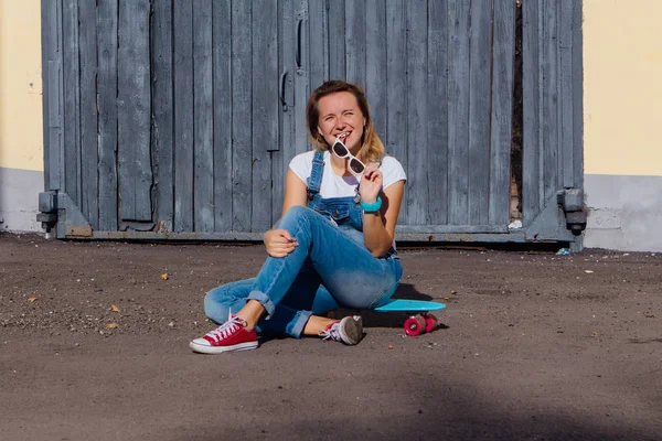 Portrait Smiling Woman Dressed Overalls Sunglasses Sitting Her Skateboard Next — Stock Photo, Image