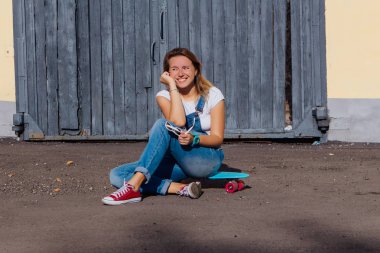 Tulum ve güneş gözlüğü eski ahşap duvar yanında onun kaykay üzerinde oturan giymiş bir gülümseyen kadın portresi.