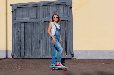 Tulum ve eski ahşap duvar yanında onun kaykay ile ayakta güneş gözlüğü giymiş bir gülümseyen kadın portresi.